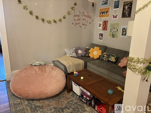 A living room decorated for Christmas with a couch, ottoman, and a garland on the wall.