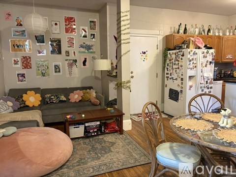 A living room with a couch, a table, a chair, a fridge, and pictures on the wall.