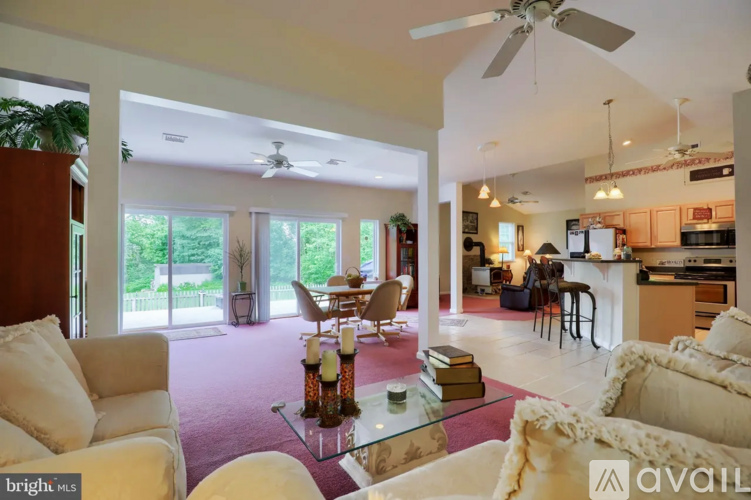 A bright living room with a glass coffee table and a kitchen in the background.