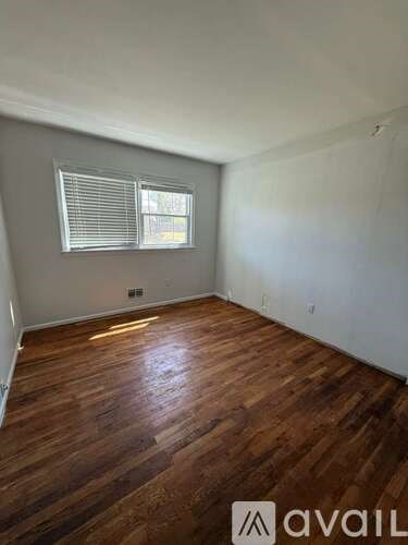 A room with wooden flooring and a window with blinds.