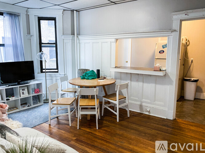 A living room with a white table and chairs, a television, and a window.