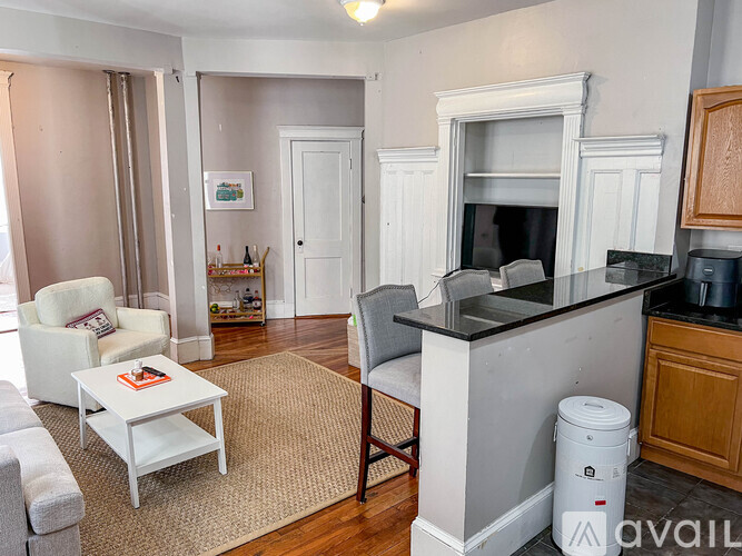 A living room with a white couch, a white coffee table, a grey chair, a fireplace, and a trash can.