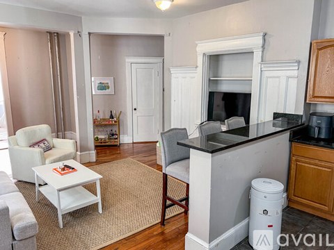 A living room with a white couch, a white coffee table, a grey chair, a fireplace, and a trash can.