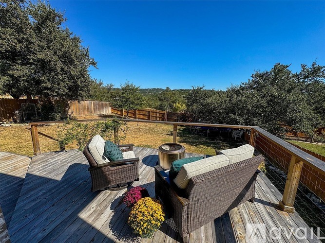 A wooden deck with two chairs and a table surrounded by a fence and trees.