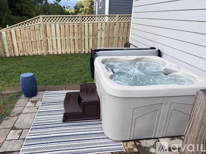A hot tub sits on a striped rug in a backyard.