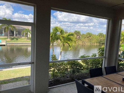 A balcony with a table and chairs overlooking a body of water with palm trees.