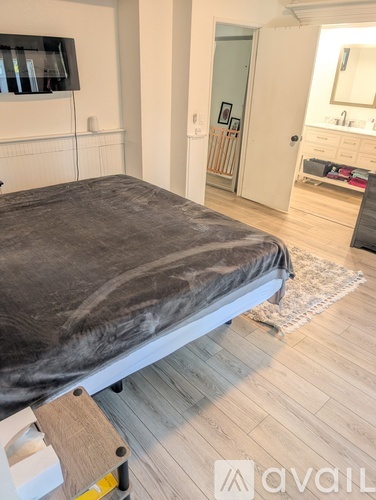 A bedroom with a bed covered in a grey blanket and wooden flooring.