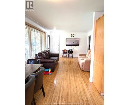 A living room with a black leather couch and a wooden floor.