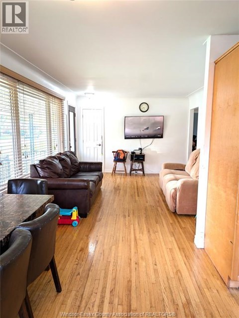A living room with a black leather couch and a wooden floor.