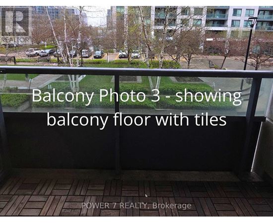 A balcony with tiled flooring and a view of a parking lot and trees.