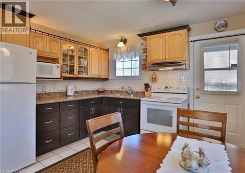 A kitchen with a white fridge and wooden chairs.