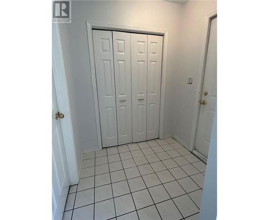 A white door with a gold handle is in a room with white walls and white tile flooring.