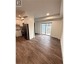 A room with a wooden floor and a kitchen area with white cabinets.