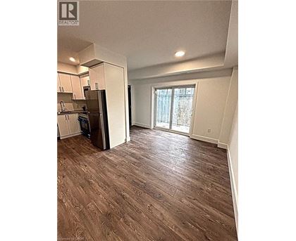 A room with a wooden floor and a kitchen area with white cabinets.