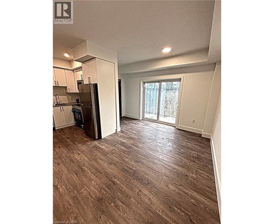 A room with a wooden floor and a kitchen area with white cabinets.