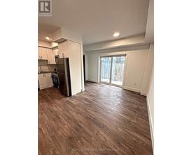 A room with wood flooring and a kitchen area with a refrigerator.