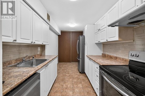 A kitchen with white cabinets and brown tiled flooring.