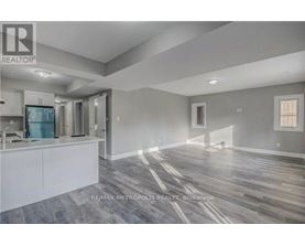 A spacious room with wooden flooring and a kitchen area with white cabinets.