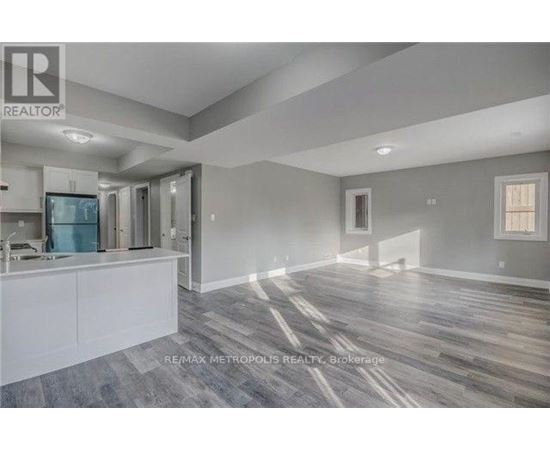 A spacious room with wooden flooring and a kitchen area with white cabinets.