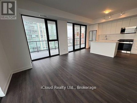 A spacious room with wooden flooring and a kitchen area with white cabinets and a stove.
