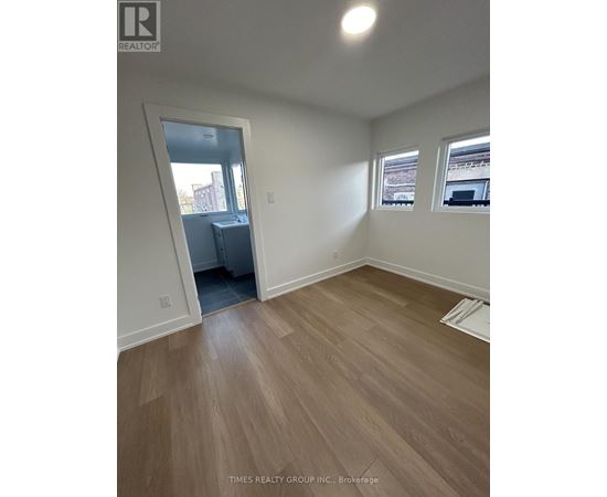 A room with wooden flooring and two windows.
