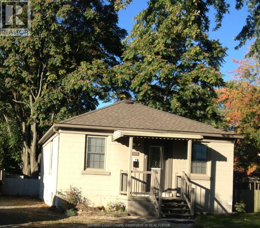 A small house with a porch and a tree in front.