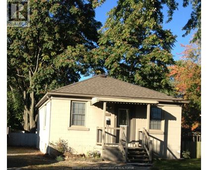 A small house with a porch and a tree in front.