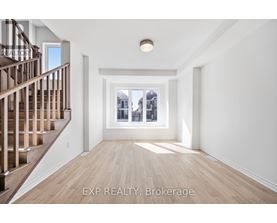 A spacious room with wooden floors and a staircase on the left side.