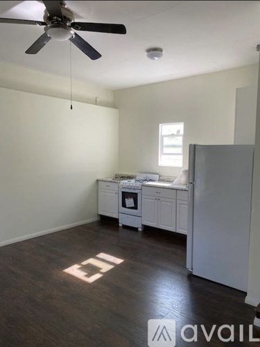A room with a fan, a refrigerator, and a small kitchenette.