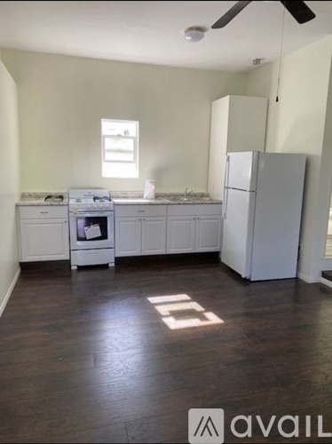 A kitchen with white appliances and cabinets, a window, and a ceiling fan.