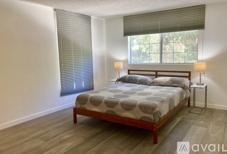 A bedroom with a bed, nightstand, and window with blinds.