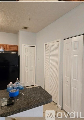 A kitchen with a black fridge, white cupboards, and a granite countertop.