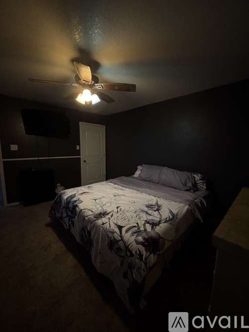 A bedroom with a bed, a ceiling fan, and a wall-mounted TV.