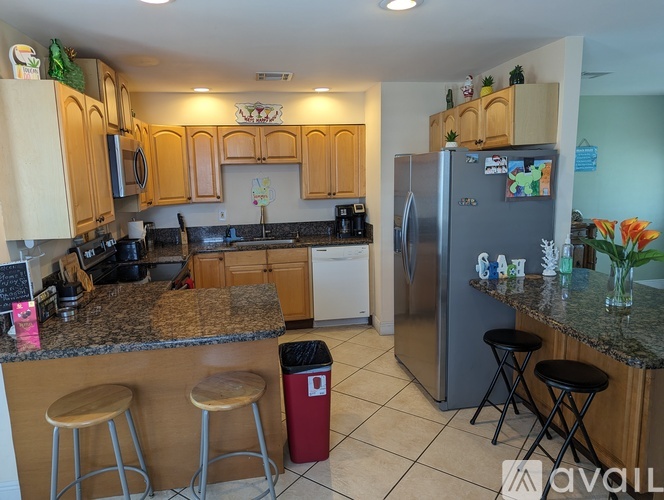 A kitchen with a refrigerator, stools, and a counter.