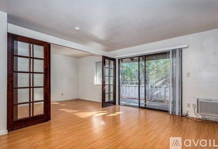 A room with wooden floors and a sliding glass door leading to a balcony.