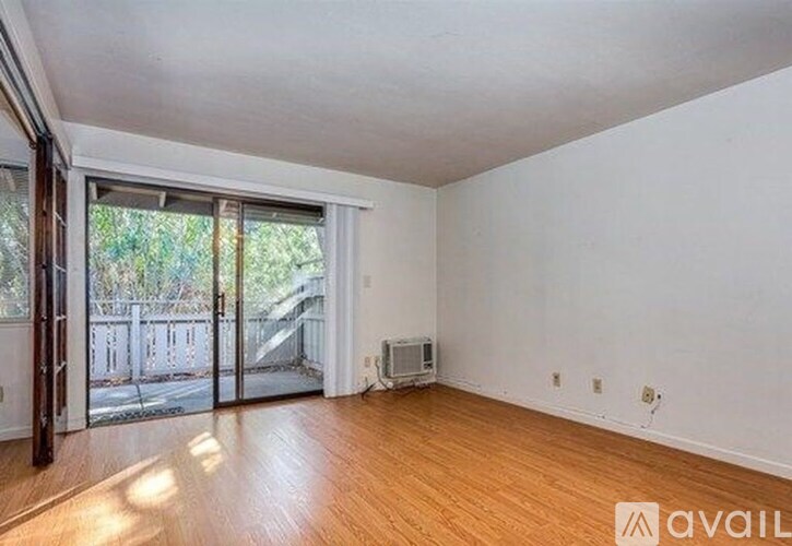 A room with wooden floors and white walls, with a sliding glass door leading to a balcony.