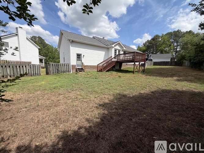 A house with a white exterior and a deck is surrounded by a fence and trees.
