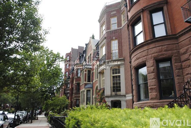 A row of brown and beige townhouses with green trees in front.