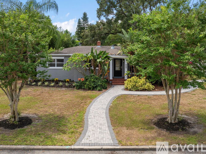 A house with a grey roof and a black door is surrounded by trees and bushes.