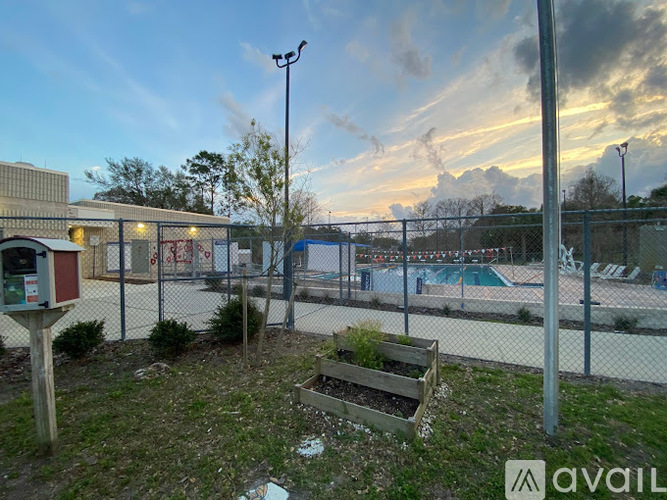 A sunset view of a pool area with a fence and a bench.