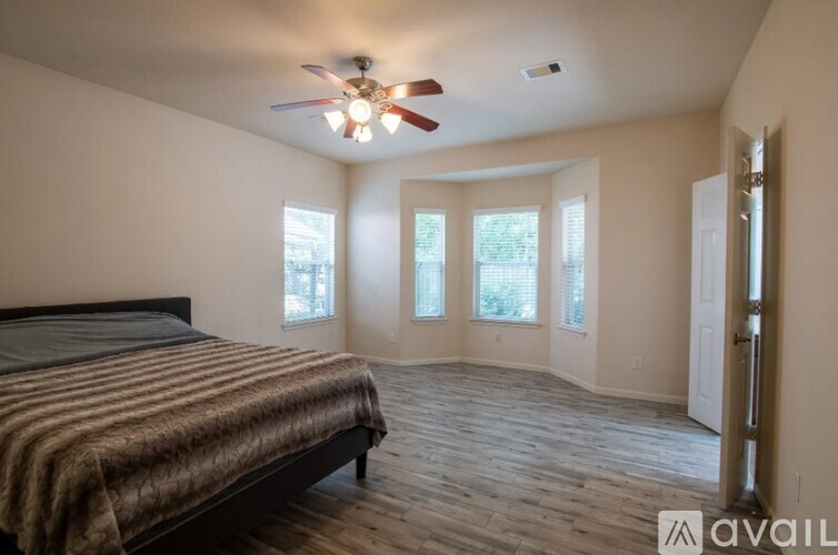 A bedroom with a bed, a ceiling fan, and a door leading to a hallway.