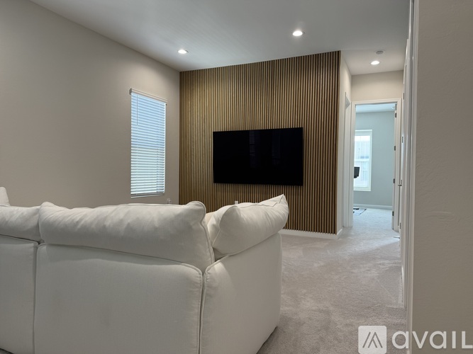 A living room with a white couch and a television mounted on the wall.
