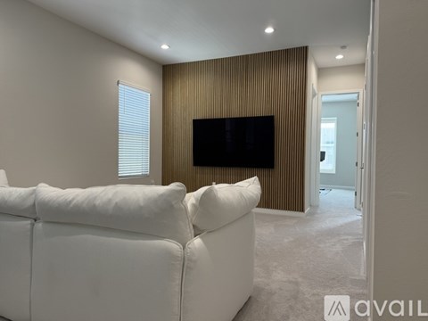 A living room with a white couch and a television mounted on the wall.