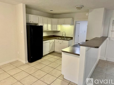 A kitchen with white cabinets and a black refrigerator.