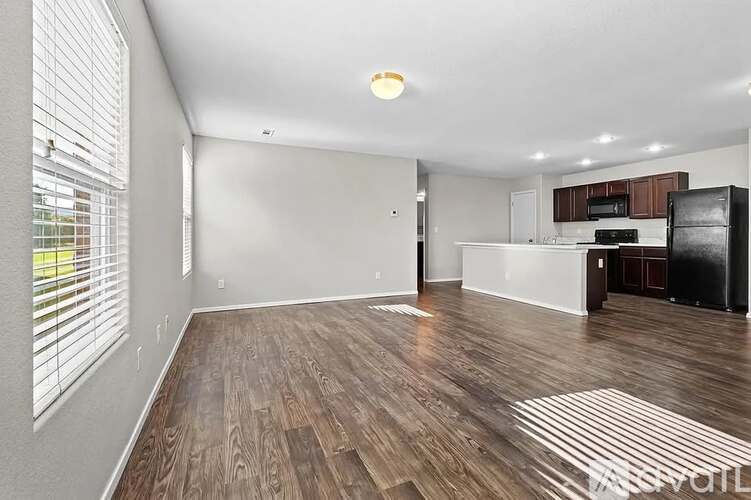 A spacious living room with wooden flooring and a kitchen area in the background.