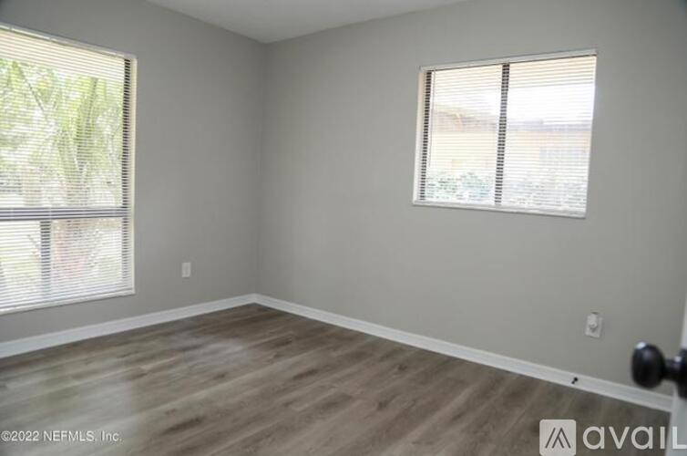 A room with wooden flooring and two windows.