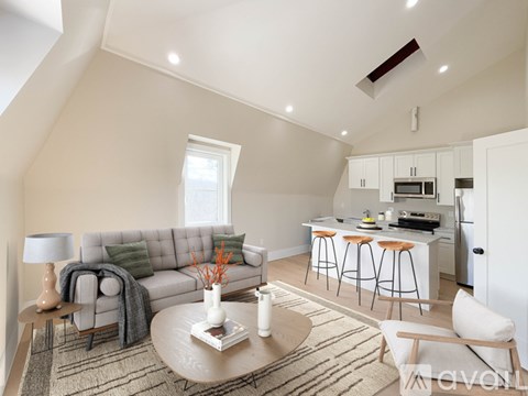 A living room with a grey couch, a coffee table, and a kitchen area in the background.