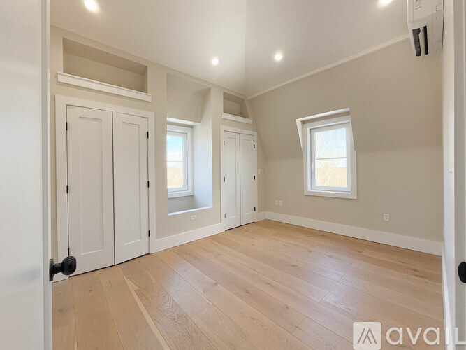 A room with wooden floors and white walls, featuring a window and a door.