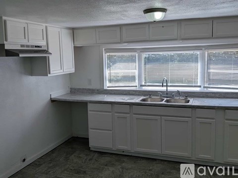 A kitchen with white cabinets and a window with blinds.