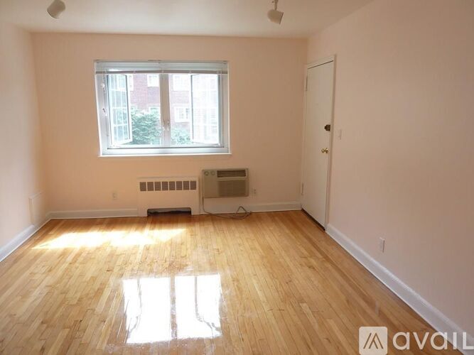 A room with wooden flooring and a window letting in sunlight.